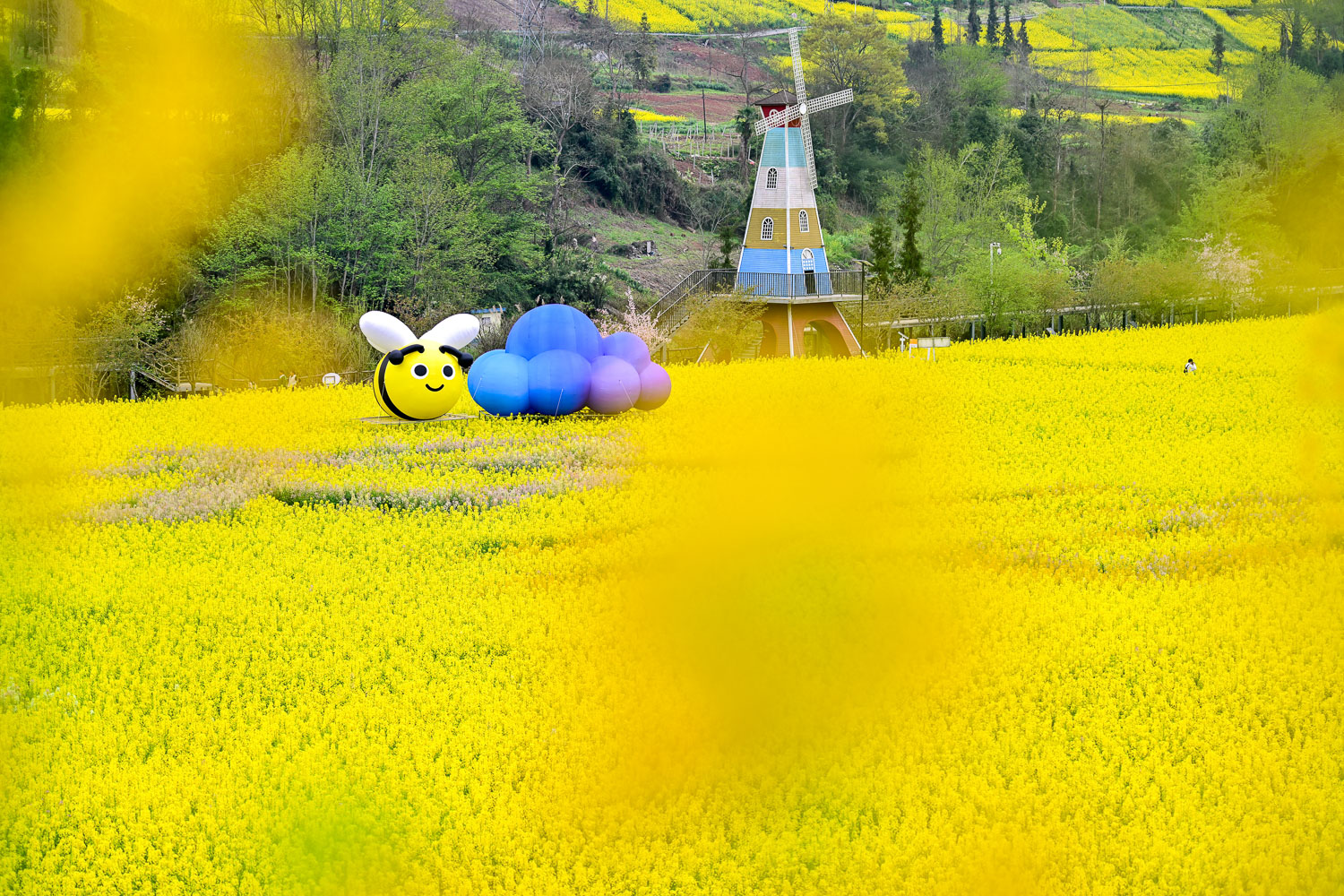 四川雅安芦山县青衣芸谷景区油菜花田春日打卡点，含卡通蜜蜂、彩色气球及风车装置，文旅商业摄影案例