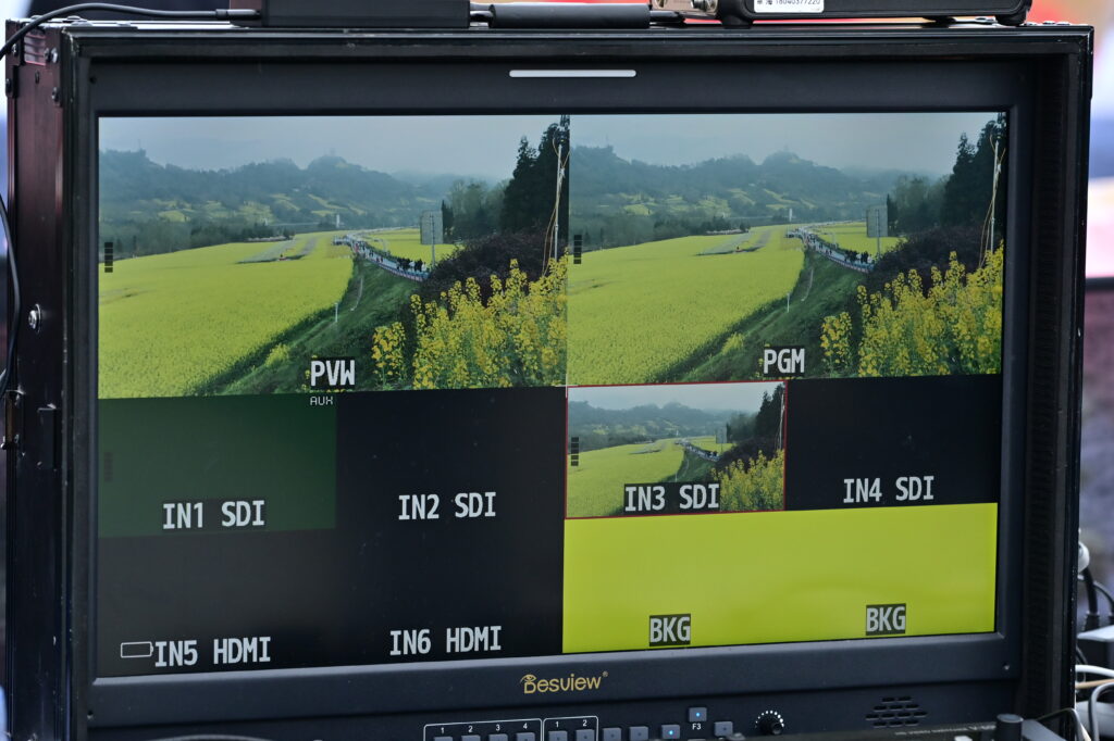 百视悦S21导演监视器四分割画面，显示四川雅安芦山县青衣芸谷景区油菜花田活动多机位实况，含PVW/PGM预览与节目输出画面，专业影视制作现场纪实